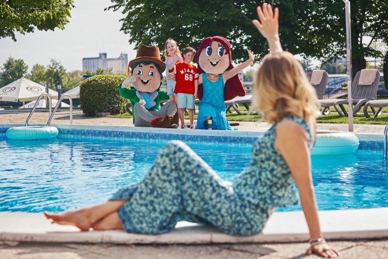 Mama sedí pri bazéne a máva deťom